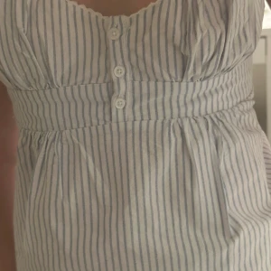 Randig blus från Brandy Melville - Supersöt blus från Brandy Melville i vit och ljusblå randigt mönster. V-ringad med tre knappar framtill, smockad midja och knytband bak. I onesize, priset kan såklart diskuteras 🩷