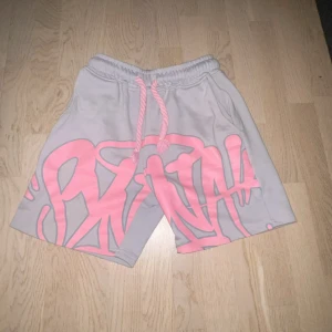 Grå syns world t shirt & shorts  - Säljer ett par grå shorts från STHLM med fett rosa graffiti-print över hela framsidan. De har bred resår i midjan och grov snörning i matchande rosa. Materialet är mjuk bomull, perfekt för chill dagar. Streetwear-vibe och riktigt snygga detaljer.