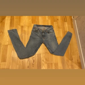 Ljusblå jeans från Nudie Jeans - Säljer ett par ljusblå jeans från Nudie Jeans med klassisk femficksdesign och snygga detaljer på bakfickan. Jeansen har en rak passform och är tillverkade i mjukt denimtyg. Perfekt för dig som gillar stilrena och tidlösa jeans.