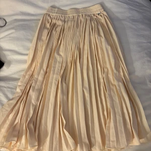 Plisserad beige långkjol från Molo - Säljer en superfin plisserad långkjol från Molo i en ljus beige nyans. Kjolen har elastisk midja och ett snyggt fall med tydliga veck. Perfekt för dig som gillar en stilren och luftig look.