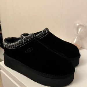 Svarta UGG boots med mönstrad kant - Säljer ett par svarta UGG boots med platt sula och rund tå. Skorna har en snygg stickad kant med vitt och grått mönster runt öppningen. Utsidan är i mjuk mocka och insidan är fodrad för extra komfort. Perfekta för kalla dagar och riktigt mysiga.