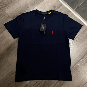 Blå Polo Ralph Lauren T-shirt  - Säljer en helt ny mörk blå Polo Ralph Lauren T-shirt med hög kvalite för väldigt bra pris. Den är helt ny med prislapp och oanvänd. Perfekt för sommaren!Det står L på tröjan som storlek men passar som S/M. Skriv vid intresse!!!!