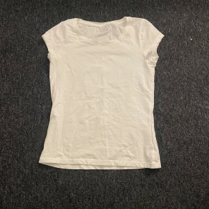 Vit t-shirt från Lindex - En enkel och klassisk vit t-shirt från Lindex med rund hals och korta ärmar. Modellen är figurnära och tillverkad i mjuk bomull, perfekt för en clean och fräsch look. Passar dig som gillar basic och stilrent.