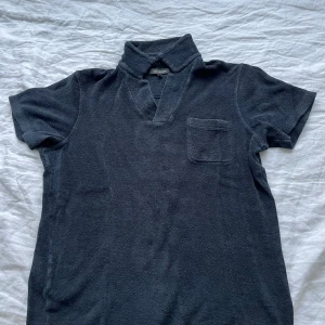 Mörkblå frotté pikétröja - Säljer en mörkblå pikétröja i mjuk frotté från Paul & Friends. Tröjan har korta ärmar, klassisk krage med öppen hals och en bröstficka. Perfekt för chill dagar eller strandhäng.