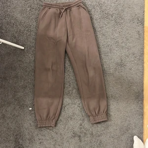 Bruna mjukisbyxor från Lindex - Bruna mjukisbyxor från Lindex med elastisk midja och snörning. Byxorna har ribbade muddar vid bensluten och är tillverkade i mjukt, fleeceliknande material på insidan. Perfekta för chill dagar och har en loose passform. Aldrig använda mer än 3gånger 