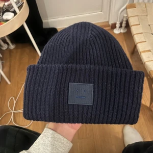 Mörkblå mössa Acne Studios - Snygg mörkblå ribbstickad mössa från Acne Studios. Tillverkad i 100% ull för extra värme och komfort. Perfekt accessoar för att lyfta din vinterstil. Nypris 1700kr.