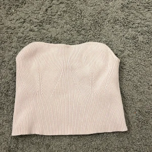 Ljusrosa ribbad tubtopp från Bershka - Säljer en ljusrosa ribbad tubtopp från Bershka. Toppen är bandeau-modell och har en snygg, tight passform med vertikala ribbade detaljer som ger en cool struktur. Perfekt att styla med jeans eller kjol för en trendig look.