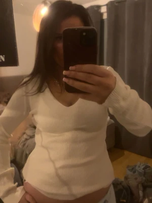 Vit ribbad långärmad tröja - Säljer en vit ribbad tröja med lång ärm och v-ringad hals. Tröjan har en figurnära passform och är perfekt för lager-på-lager. Enkel och stilren design som passar till det mesta.