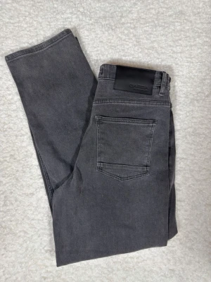 Grå jeans från Gabba med rak passform - Snygga grå jeans från Gabba med klassisk femficksdesign och rak passform. Jeansen har en mörkgrå ton och är tillverkade i mjukt bomullsmaterial. Perfekta för en avslappnad och stilren look.