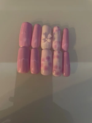 Rosa press-on naglar med rosett - Säljer ett set press-on naglar i rosa med blommor och rosett. En nagel har en söt 3D-rosett som detalj. Det är mitt första set därav inte det bästa!💗