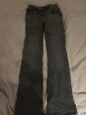Grå bootcut jeans med låg midja - Säljer ett par gråa bootcut jeans med låg midja. Jeansen har klassisk femficksdesign och är tillverkade i ett mjukt denimtyg. Perfekta för dig som gillar en avslappnad och retro look.