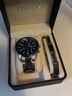 Citizen klocka med blå urtavla - Stilren Citizen klocka med blå urtavla, silverfärgad boett och länkarmband i rostfritt stål. Klockan har kronograf och tachymeter, samt tydliga vita siffror. Extra länk medföljer för justering av armbandet. Perfekt accessoar för dig som gillar klassisk design. Kom privat om priset ejj fungerar