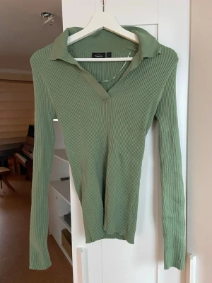 Grön ribbad tröja med krage - Snygg grön ribbad tröja från KappAhl med lång ärm och klassisk krage. Tröjan har en djup v-ringning och är figurnära i modellen, vilket ger en trendig och stilren look. Perfekt att matcha med jeans eller kjol för en cool vardagsstil. Otroligt mjuk och skön och mycket stretchig så den passar nog en strl M också!💚