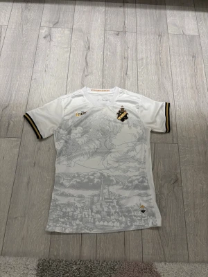 Vit AIK matchtröja från Nike - Snygg vit AIK matchtröja från Nike med gulddetaljer och klubbmärke på bröstet. Tröjan har ett unikt tryck med Stockholmsmotiv och texten 'STOCKHOLMENSIS' i nacken. Tillverkad i ett lätt och ventilerande material, perfekt för fotboll eller träning. Helt ny utan prislapp aldrig använd. Pris kan diskuteras!