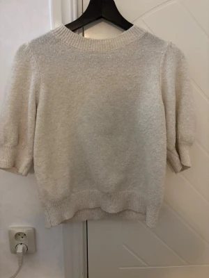 Beige stickad tröja Vero Moda XS - Mysig beige stickad tröja från Vero Moda i storlek XS. Tröjan har puffiga korta ärmar och ribbade muddar vid hals, ärmslut och nederkant. Perfekt för dig som gillar en enkel men ändå trendig look.