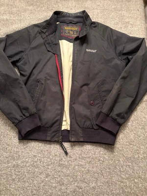 vindjacka från Woolrich - Klassisk svart vindjacka från Woolrich med diskret logga på bröstet. Jackan har dragkedja, ribbade muddar och krage samt två snedställda fickor fram. Insidan är ljus och jackan har en sportig, tidlös look som passar till det mesta.