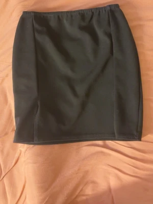 Svart kortkjol med slits - En svart, enkel och stilren kortkjol med liten slits på båda sidorna. Kjolen har rak passform och resår i midjan, vilket gör den bekväm och lätt att bära. 