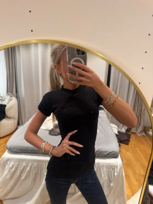 Svart tight t-shirt i bomull - Enkel och stilren svart t-shirt med tight passform och korta ärmar. Tillverkad i mjuk bomull, perfekt att matcha med jeans eller kjol. Klassisk rund halsringning och utan synliga loggor eller tryck.