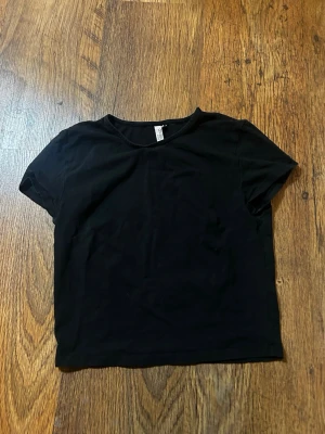 Svart basic t-shirt från nly trend - En enkel svart t-shirt från nly trend med rund hals och korta ärmar. Modellen är croppad och har en clean, minimalistisk look som passar till allt. Tillverkad i mjuk bomull för skön känsla hela dagen.