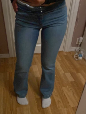 Blå bootcut jeans  - Säljer ett par ljusblå bootcut jeans med klassisk femficksdesign och knappgylf. Jeansen har en bekväm passform och är tillverkade i mjukt bomullsmaterial. Man kan vika upp och ha högmidjat eller så har man dom som jag har på bilden lite lågmidjade