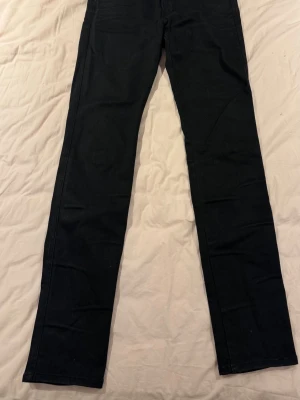 Svarta Replay Anbass jeans - Säljer ett par svarta Replay Anbass jeans i klassisk femficksmodell. Jeansen har smal passform, raka ben och snygga detaljer vid fickorna. Materialet är stretchigt jeans för extra komfort och de har en stilren look med svarta sömmar och Replay-logga på bakfickan.