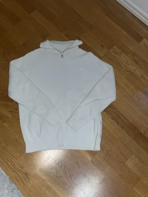 Vit ribbad half zip-tröja Calvin Klein - Säljer en stilren vit ribbad tröja från Calvin Klein med half zip och diskret CK-logo på bröstet. Tröjan har lång ärm och hög krage, perfekt för lager på lager. Skön och mjuk känsla, passar till allt.