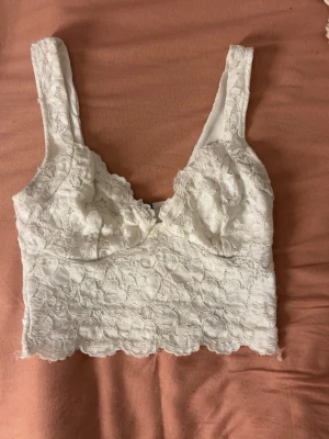 Vit spetsig croppad topp - Superfin vit croppad topp i spets och breda axelband. Snyggt mönstrad spets över hela toppen och v-ringad skärning framtill. 