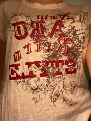 Vit t-shirt med röd glittertext - Cool vit t-shirt med röd glittrig text och tryck framtill. T-shirten har korta ärmar och rund halsringning. Priset går att diskutera! 