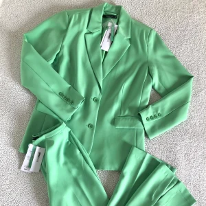 Ginatricot grön kostym med kavaj och kostymbyxor - Otroligt snygg livligt grön kostym från Ginatricot med oversize kavaj och lågmidjade kostymbyxor. Nytt med prislappar. Storlek XS i båda delar men säljer även byxorna i storlek S. Ordinariepris: 1100kr