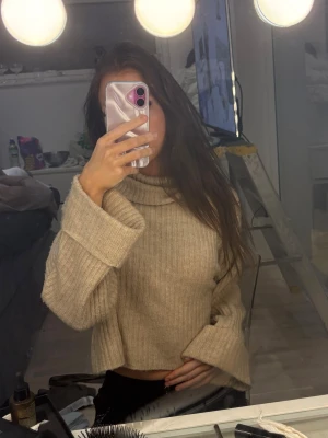 Beige ribbad polotröja Gina Tricot - Mysig beige polotröja från Gina Tricot i ribbstickat material. Tröjan har en hög krage, croppad passform och långa ärmar med breda muddar. Perfekt för lager på lager under höst och vinter.