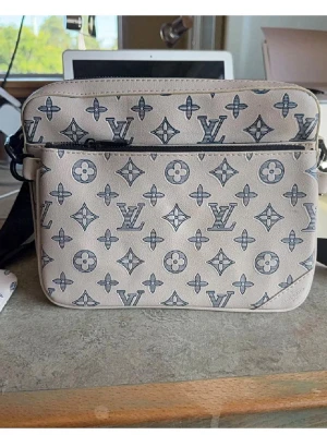 Beige Louis Vuitton monogramväska - Säljer en beige axelväska från Louis Vuitton med klassiskt monogrammönster i svart. Väskan har justerbar svart axelrem, dragkedja upptill och en extra liten ficka framtill. Materialet är slätt och känns lyxigt, perfekt för dig som gillar designeraccessoarer.
