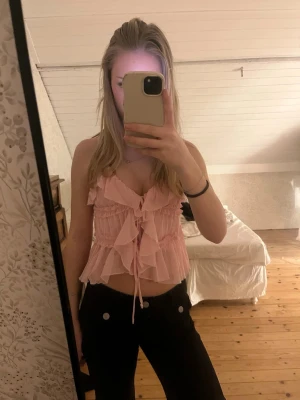 Ljusrosa volangtop med knyt - Supersöt ljusrosa topp med volanger och knyt framtill. Toppen har smala axelband och en luftig, flowy passform. Perfekt för varma dagar och ger en romantisk vibe till outfiten.💓