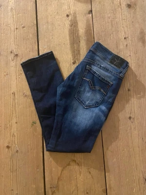 Replay jeans i mörkblå w28 L30 - Säljer ett par snygga Replay jeans i mörkblå tvätt med slitningar och skinny passform. Klassisk femficksmodell med coola detaljer på bakfickorna. Jeansen är gjorda i stretchig bomull för skön komfort och har låg midja. Perfekta för dig som gillar en smal siluett.
