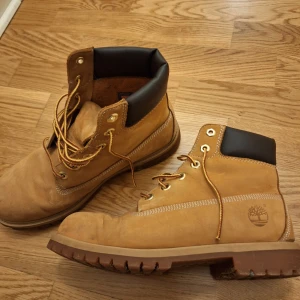 Timberland boots i beige mocka - Säljer ett par klassiska Timberland boots i beige/orange mocka med bruna detaljer vid ankeln och grov sula. Skorna har rund tå, snörning med gulbruna skosnören och metallöglor. Timberland-loggan är präglad på sidan. Perfekta för höst och vinter. Skorna är i använt skick och kan behöva en ny innersula för comfortens skull! I övrigt är skon i bra skick men somsagt använd! Används tyvärr inte här hemma längre men älskar dem!💗