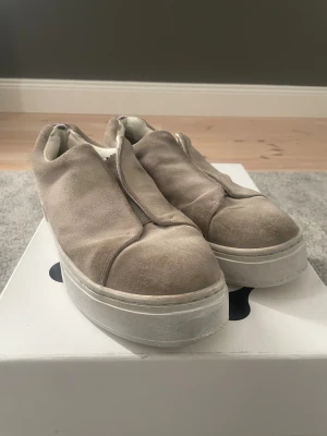 Beige Eytys sneakers i mocka - Säljer ett par Chunky sneakers från Eytys i beige mocka med bred vit plattformsula. Skorna har minimalistisk design utan synlig snörning. Det enda slitaget skorna har är två små hål på vardera häl som går att se på bild 1, utöver det är det bara möjligtvis en tvätt som skulle behövas. Skorna och originalkartongern är det som ingår. Perfekta för dig som gillar stilren och modern streetwear. Nypris 2000kr. Pris går att diskutera.