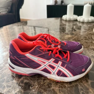 Lila och rosa sneakers från Asics - Snygga sneakers från Asics i lila mesh med rosa detaljer och snörning. Skorna har vit sula med rosa inslag och den klassiska Asics-loggan i vitt på sidan. Perfekta för träning eller vardagsstil.