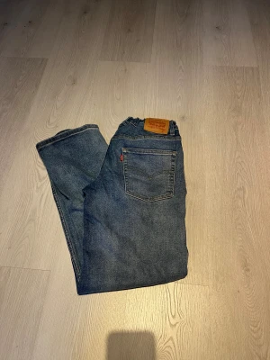 Levi's 501 blå jeans straight fit - Säljer ett par klassiska Levi's 501 jeans i blå tvätt med raka ben och normal passform. Jeansen har fem fickor, gul kontrastsöm och den ikoniska läderpatchen bak i midjan. Perfekt för dig som gillar tidlös denimstil.