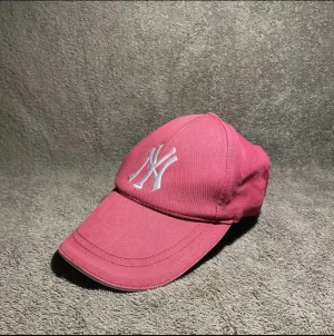 Rosa New York Yankees keps - Snygg rosa keps från New York Yankees med vit broderad NY-logga framtill. Justerbar rem baktill för perfekt passform. Klassisk böjd skärm och tillverkad i bomullstyg som andas. Perfekt accessoar för en sportig och trendig look.