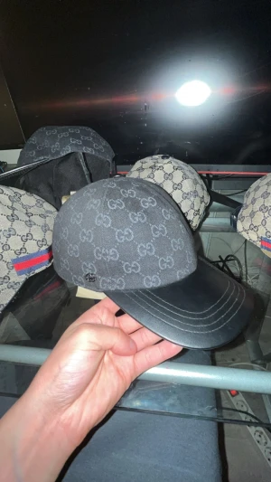 Svart Gucci keps med GG-mönster - Snygg svart keps från Gucci med klassiskt GG-monogram i grått över hela kepsen. Skärmen och justerbar rem baktill är i svart skinn. Kepsen har en metallogo framtill och insida med Gucci-etikett. Perfekt för dig som vill ha en lyxig och stilren accessoar.
