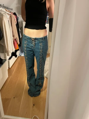 Coola jeans med snörning  - Unika blå jeans med snygg snörning längs hela framsidan och vid midjan. Modellen är lågmidjad och har raka ben med en utsvengling längst nertill med normal passform. Jeansen är tillverkade i stretch denim och har bakfickor. 