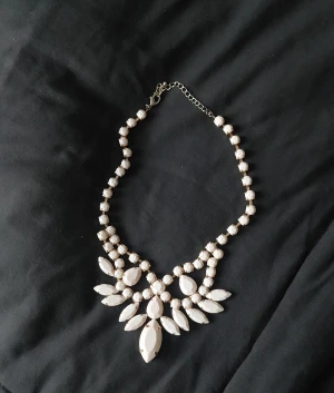 Statement halsband med rosa stenar - Snyggt statement halsband med stora rosa stenar i olika former, satta i guldfärgad metall. Halsbandet har justerbar kedja och ett iögonfallande, elegant mönster framtill. Perfekt för att lyfta vilken outfit som helst.