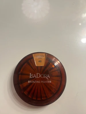 IsaDora Bronzing Powder Golden Tan - IsaDora Bronzing Powder i nyansen 46 Golden Tan. Kommer i en rund, brun plastförpackning med spegel i locket. Ger en solkysst look med en varm, gyllene ton. Perfekt för att framhäva ansiktskonturer och skapa glow. Fragrance free och kliniskt testad.