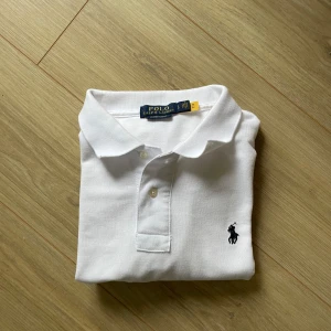 Piké Ralph Lauren  - Klassisk vit pikétröja från Polo Ralph Lauren med broderad logga på bröstet. Tröjan har korta ärmar, krage och två knappar framtill. Tillverkad i bomull för en skön och luftig känsla. Perfekt för en clean och stilren look. Tröjan är helt ny, säljer då den inte passar mig.