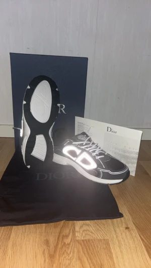 Svarta Dior b30s - Säljer ett par svarta Dior sneakers med vit sula och reflekterande CD-logga på sidan. Skorna har snörning och en rund tå, samt snygga kontrastdetaljer i vitt. Materialet är en mix av syntet och skinn, vilket ger en lyxig och modern vibe. Perfekt för dig som gillar exklusiva märken.