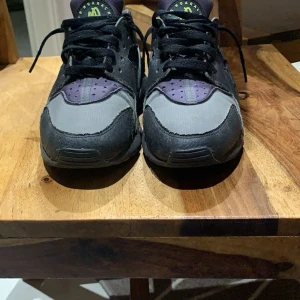 Nike Air Huarache sneakers svart/lila - Nike Air Huarache sneakers i svart och lila med cool design och detaljer i syntet och textil. Skorna har snörning, rund tå och en unik hälkappa i plast. Perfekta för dig som vill sticka ut med en sportig och urban look.