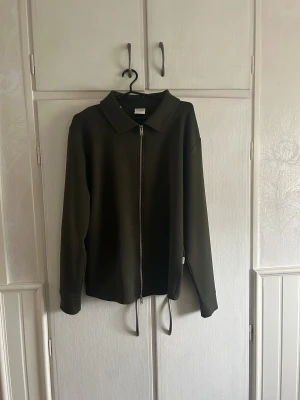 Grön overshirt från Selected Homme - Använd Max 1 gång Stilren mörkgrön overshirt från Selected Homme med rak passform, klassisk krage och hel dragkedja framtill. Jackan har långa ärmar och är tillverkad i ett mjukt material som känns skönt mot huden. Perfekt att slänga över en t-shirt för en clean look.