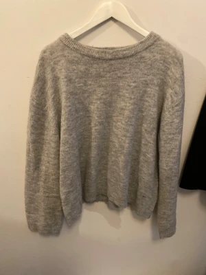 Grå stickad tröja med rund hals - Mysig grå stickad tröja med rund halsringning och långa ärmar. Perfekt för kyliga dagar och enkel att matcha med jeans eller kjol. Tröjan har en avslappnad passform och ribbade muddar vid ärmslut och hals.