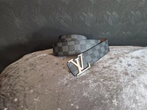 Svart Louis Vuitton skärp i skinn - Snyggt svart skärp från Louis Vuitton med klassisk LV-logga i guld som spänne. Bältet har präglade LV-mönster längs hela remmen och är gjort i exklusivt skinn. Perfekt accessoar för att lyfta din outfit.