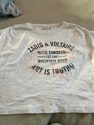 Grå Zadig & Voltaire t-shirt med tryck - Säljer en grå t-shirt från Zadig & Voltaire med coolt svart tryck och texten 'ART IS TRUTH' samt rosa blommönster i bakgrunden. 