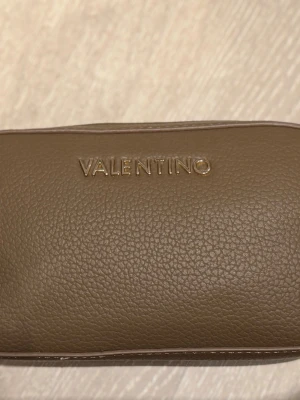  Valentino väska - Valentino väska i brun färg. Väskan har en kompakt design med dragkedja och ett medföljande axelband. 